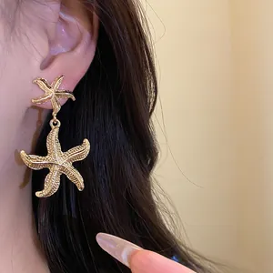 Close-up of golden starfish dangle earrings with a textured wrinkled metal finish.