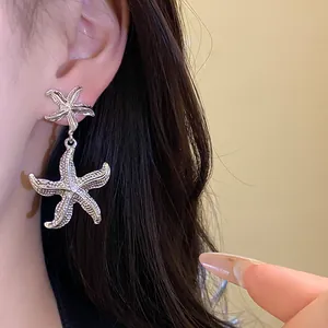 Macro view of textured silver starfish drop earrings worn on ear with dark hair.