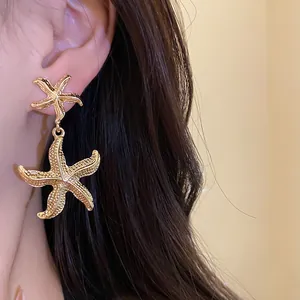 Detail showing elegant golden wrinkled starfish drop earrings worn on a model ear