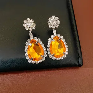 Detail view of orange pear-shaped drop earrings with sparkling rhinestone halo design.