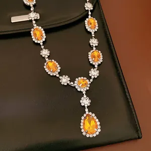 Detailed macro shot of an orange teardrop and oval rhinestone necklace on black leather.