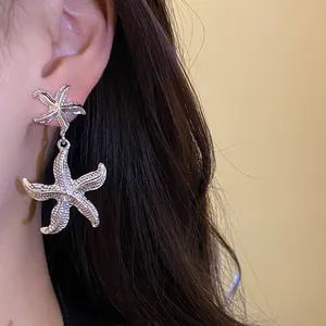 Detailed close-up showing elegant silver textured starfish drop earrings on a model's ear.