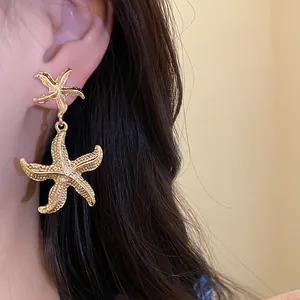 Detailed close-up showing gold metal wrinkled starfish drop earrings worn on an ear