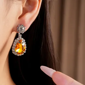 Close-up detail of luxury teardrop rhinestone earrings with a large orange amber stone