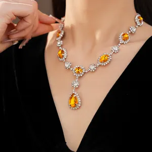 Close-up of elegant silver necklace with vibrant orange teardrop and oval rhinestones.