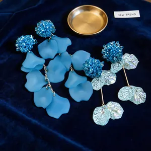 Close-up view of blue acrylic petal earrings and iridescent leaf drops on blue velvet.