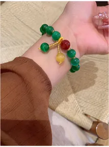 Détail d'un bracelet en perles d'oeil de chat vert avec des pendentifs colorés au poignet