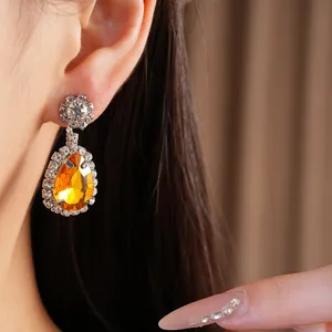 Close-up of elegant amber teardrop dangling earring with rhinestone halo on model ear