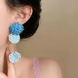 Close-up of blue beaded flower and crackle petal dangle earrings on model