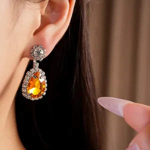 Detailed close-up showing a sparkling orange teardrop crystal earring worn by a model