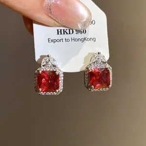 Close-up of elegant red square zircon earrings with shimmering halo and leaf detail.