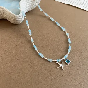 Detail of summer style necklace featuring a silver starfish and square blue gem pendant.