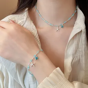 Close-up of a blue bead necklace and bracelet set with silver starfish pendants worn by a model
