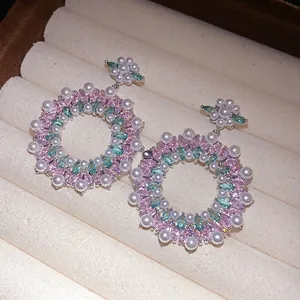 Floral wreath drop earrings featuring pink and teal zircon with pearls on a cream display box