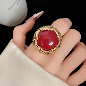 Close-up van vintage ronde rode harsring met een getextureerd gouden montuur op de hand