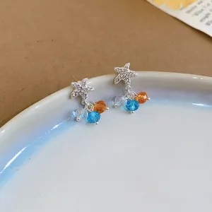 Macro detail shot of starfish stud earrings featuring vibrant blue and orange faceted crystals