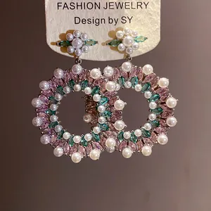 Detailed view of luxury silver needle earrings with pink and green zircons and white pearls.
