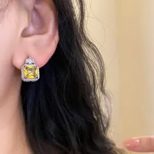 Macro view of a square yellow zircon earring with clear pavé stones on a female model's ear