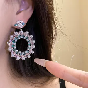 Detailed macro view of ornate zircon and pearl circular drop earrings worn on ear.