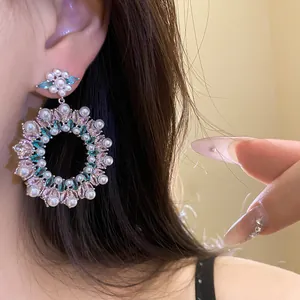 Detailed macro view of ornate floral zircon and pearl hoop earrings worn on ear