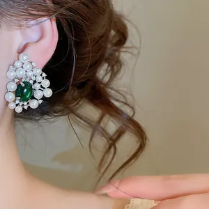 Detailed view of elegant vintage-style pearl earrings with a green stone on model