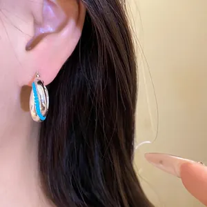 Minimalist silver hoop earrings featuring vibrant blue bead inlay detail on model ear