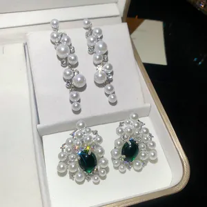 Close-up of elegant white resin pearl earrings featuring striking green gemstone accents