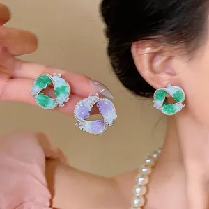 Macro detail of geometric swirl stud earrings featuring crushed green and purple stones.