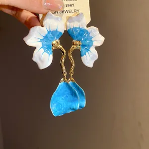Close-up of blue and white enamel flower earrings with gold wavy stems and petal drops.