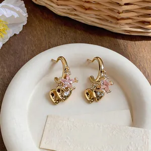 Detail shot of elegant gold C-shape hoop earrings featuring pink star and heart zircon charms
