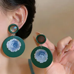 Detailed macro view of vintage French green circular earrings with blue resin rose petals.