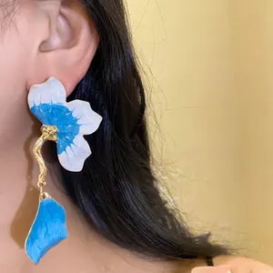 Close-up detail of blue and white enamel flower earrings with a gold-toned petal drop