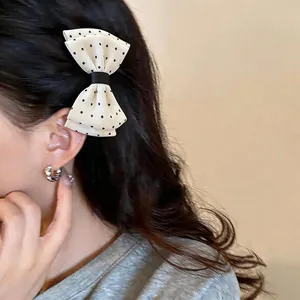 Dettaglio laterale di un'elegante clip per capelli a fiocco con pois beige su capelli scuri