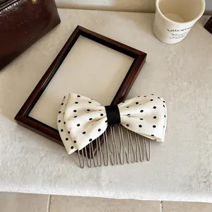 Dettaglio di un pettine per capelli con fiocco in tessuto a pois bianchi su sfondo.