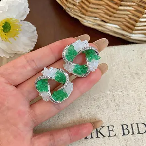 Close-up of geometric stud earrings with green glass and pavé-set zircons