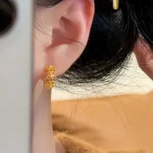 Detaillierte Nahaufnahme von hohlen Goldohrringen mit Spitzenblumen am Ohr