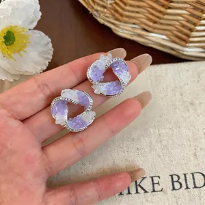Detailed macro view of geometric stud earrings featuring purple glass and pavé crystals