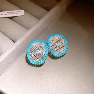 Close-up detail of silver-plated mesh stud earrings with blue beads and sparkling zircons