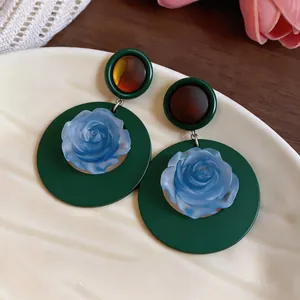 Macro view of vintage French style blue rose stud earrings with a dark green circular base