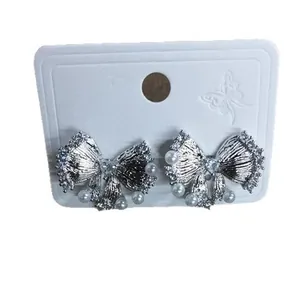Pendientes de lazo plateados con perlas y strass en una tarjeta de exhibición.