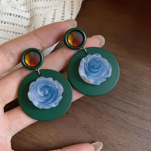 Detailed macro view of vintage dark green round earrings with light blue resin rose.