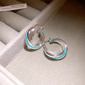 Close-up detail of silver-toned twisted hoop earrings with turquoise beads on a gray tray.