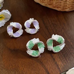 Detail shot showing geometric silver earrings with purple and green glass stone textures.