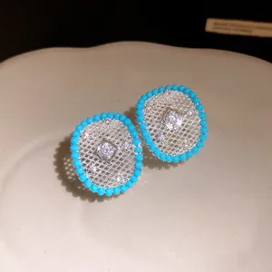 Close-up of silver hollow mesh stud earrings with turquoise bead border and zircon center