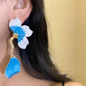 Close-up of vibrant blue and white enamel flower petal drop earrings with gold stem