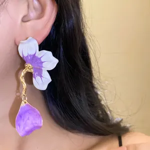 Close-up detail of white and purple enamel floral earrings worn on a model's ear.