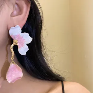 Macro detail of elegant pink oil-drop flower earrings with dangling petal on a model