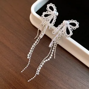 Macro detail of zircon lace bow earrings with elegant long silver chain tassels