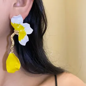 Detail view of vibrant yellow and white enamel flower petal drop earrings on model