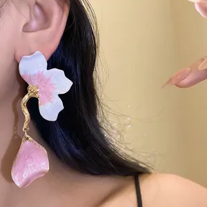 Detailed close-up of sweet pink and white enamel flower petal drop earrings on model.